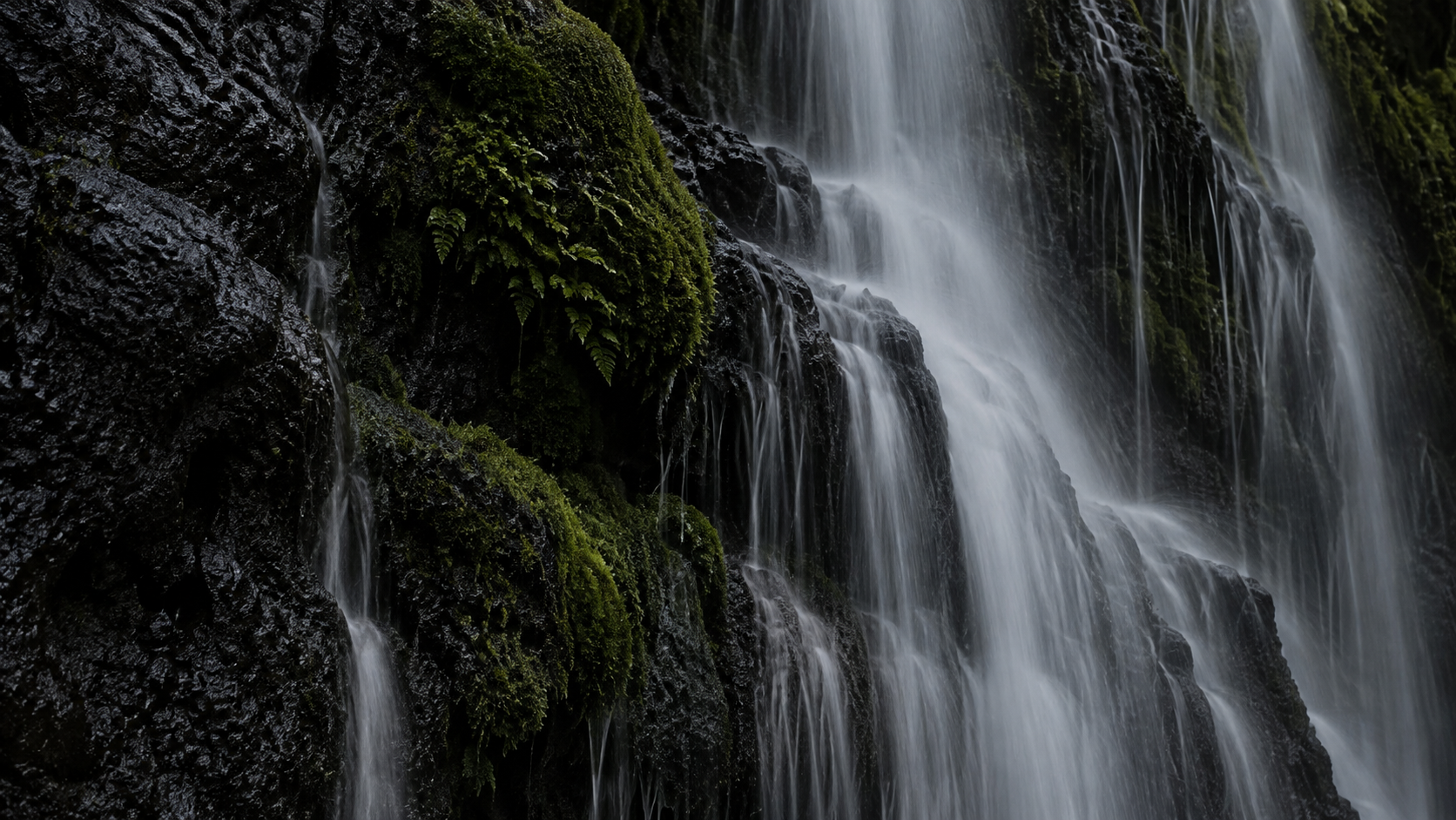 Water falling over dark stone and moss.
